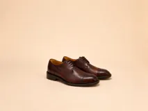 Zapato de vestir estilo oxford en cuero vacuno color marrón oscuro, con puntera reforzada y cierre mediante cordones. Diseño artesanal con suela de cuero y acabado pulido.