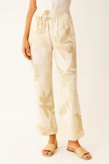 Pantalón de algodón color beige con estampado de hojas tropicales en tonos más oscuros de beige. Tiene cintura elástica, corte ancho y calce alto, con bolsillos laterales y terminación deshilachada en los tobillos.