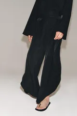 Pantalón de tiro medio confeccionado en hilatura de viscosa, de pierna ancha con pinzas en el delantero y bajo con abertura lateral. Cierre con cremallera oculta en costura.