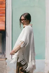 Poncho liviano de tejido de punto color blanco, con bordes decorados en crochet multicolor y flecos en el ruedo.