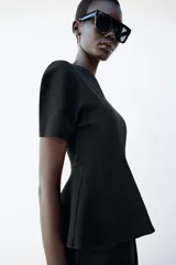 Top peplum confeccionado en hilatura de algodón de color bordó, con escote en V pronunciado, mangas cortas abullonadas y bajo con vuelo.