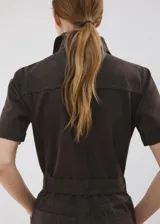 Enterito largo de algodón estilo tejano, color marrón, con cuello camisero, mangas cortas, cierre frontal con cremallera y cinturón ajustable en la cintura.