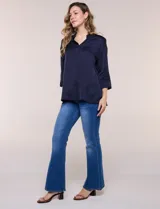 Camisa de satén azul marino con cuello mao, escote en V y mangas tres cuartos con hombro caído. Presenta silueta holgada, cierre frontal con botones y ruedo asimétrico.