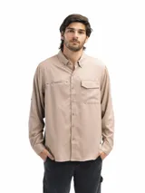 Camisa color beige de manga larga con cuello abotonado, dos bolsillos frontales con solapa y cierre de velcro, y abertura en la espalda para ventilación. Las mangas tienen presilla con botón para sujetarlas arremangadas.