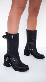 Bota de cuero negra con caña media, punta cuadrada y taco bajo. Presenta correas con hebillas metálicas y tachas plateadas.