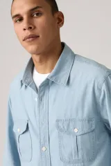 Camisa celeste de jean con dos bolsillos frontales con solapa y cierre de botón.