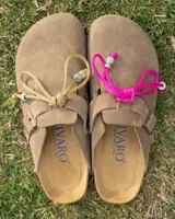Zuecos de gamuza color beige con diseño de punta cerrada y ajuste lateral mediante tira con hebilla metálica grabada. Presentan una plantilla anatómica de corcho y látex, con suela de goma antideslizante.