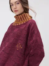 Pullover de punto jacquard con diseño de cuadros en relieve, cuello alto y mangas largas. Presenta detalles de pespuntes en color rojo en el cuello y los puños, aberturas laterales y logo bordado en el pecho.