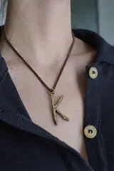 Collar de tiento de cuero marrón con dije en forma de letra y placa metálica con la inscripción de la marca.