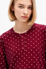 Pijama bordó con estampado de lunares blancos, compuesto por una remera de manga larga con cuello redondo y botones frontales y un pantalón largo de corte recto con cintura elástica.