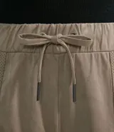 Pantalón estilo jogger de suedine, con cintura elástica y cordón ajustable, puños elásticos en los tobillos, bolsillos laterales y detalles perforados en los laterales y bolsillos.