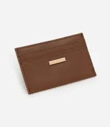 Portatarjetas pequeño de color marrón, confeccionado en poliuretano (PU) con textura lisa. Presenta tres ranuras visibles para tarjetas y una placa metálica dorada con el logo de la marca en el frente.