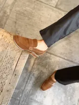 Mocasín de gamuza color marrón claro con detalle de hebilla y suela clara.