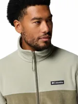 Campera polar Columbia modelo Steens Mountain con cierre frontal completo, cuello alto y bolsillos laterales con cierre. Presenta un diseño de bloques de color en tonos verde claro y verde oliva, con el logo de la marca bordado en el pecho.
