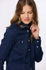 Camisa de jean azul oscuro con lycra, corte entallado, cuello clásico, cierre frontal con botones metálicos, dos bolsillos con solapa abotonada en el pecho y mangas largas con puños abotonados.