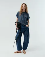 Remera blanca de lino con cuello mao, media cartera con broches metálicos y manga japonesa. Presenta un bolsillo frontal tipo plaqué, recortes laterales en sisa con detalles de encaje y ruedo redondeado con corte escalonado.