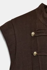 Mono largo marrón de cuello subido y manga sisa, con cierre frontal de botones metálicos dorados decorativos, cinturón ajustable del mismo tejido y bolsillos delanteros.