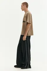 Remera de algodón de punto pesado con efecto lavado, color beige/tostado. Presenta un corte boxy (holgado) con cuello redondo ribeteado y bajo recto. Estampado frontal en negro con texto "Club Issue" y gráficos de banderas a cuadros.