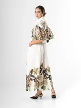 Conjunto de dos piezas confeccionado en viscosa con estampado floral en tonos marrones y verdes sobre base blanca. Incluye una blusa tipo camisa corta con cuello solapa, cierre frontal de botones y mangas abullonadas con diseño globo, y un pantalón tipo culotte de tiro alto, amplio y fluido con pinzas en la cintura.