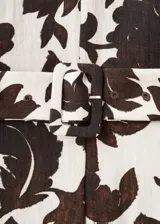 Jardinera enterito de corte recto y largo, con estampado floral en tonos marrón y fondo beige. Presenta cuello en V, manga corta, cinturón incorporado con hebilla en la cintura y cierre de cremallera en la parte posterior.