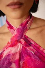Vestido midi con estampado abstracto en tonos fucsia, rosa y violeta. Presenta un diseño de cuello halter cruzado con detalle de collar integrado y espalda descubierta.