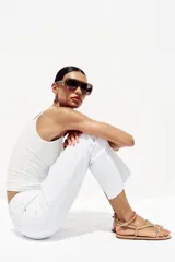 Sandalias planas color beige con tiras finas y pulsera al tobillo, decoradas con tachas metálicas doradas.