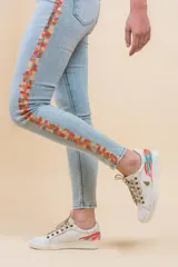 Jeans ajustados de denim celeste, con diseño pintado a mano en el lateral con una franja abstracta en tonos cálidos como rojo, naranja y amarillo.