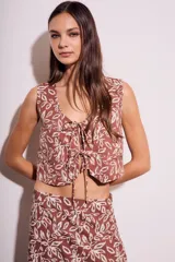 Chaleco marrón con estampado de hojas blancas, escote en V y lazos ajustables en el frente.