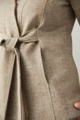 Chaqueta corta color beige, entallada, con escote en V, manga larga y bolsillos escondidos. Cierre frontal con lazo fijo. Confeccionada en lana fina sin teñir. Diseño exclusivo de Don Baez.