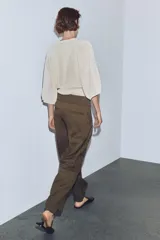Pantalón cargo de tiro medio en color marrón, confeccionado con mezcla de lana. Presenta cintura con detalle de vuelta, pliegues frontales, bolsillos laterales y bolsillos con solapa en las piernas. Cierre frontal con cremallera, botón y ganchos metálicos.