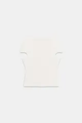 Top liso de punto color blanco crudo, con cuello barco y mangas cortas que presentan aberturas tipo cut-out.