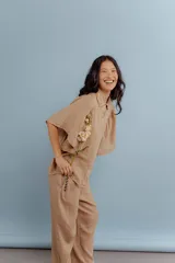 Camisa de lino color tostado, con cuello camisero y cierre frontal de botones. Se caracteriza por sus mangas cortas amplias y voluminosas que aportan un diseño fresco y liviano.