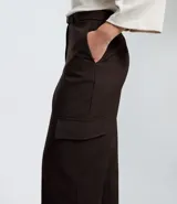 Pantalón de sastrería color marrón oscuro, de corte recto y tiro alto. Presenta bolsillos cargo laterales, trabillas para cinturón y viene con un cinturón de tela con hebilla metálica ajustable.