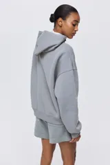 Buzo tipo canguro de corte holgado con hombros caídos, capucha de doble capa y bolsillo frontal tipo canguro. Presenta puños y bajo acanalados con interior suave.