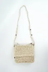 Bandolera beige de tejido rústico estilo crochet con solapa, correa larga con cuentas de madera decorativas y cierre superior.