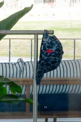 Gorra con estampado animal print en tonos azules y grises, con bordado de serpiente roja en el frente. Tiene visera y ajuste trasero con pasador.