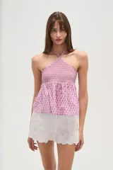 Top sin mangas confeccionado en algodón con estampado integral en tonos rosados. Presenta un diseño con cuello halter cruzado, pechera elástica con técnica de nido de abeja y bajo con volado tipo peplum.