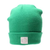 Gorro tipo beanie de tejido de punto en color verde, con vuelta en el borde y etiqueta frontal cuadrada con texto circular en color rosa.