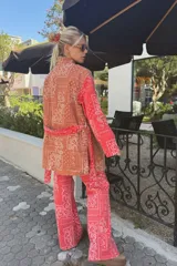 Kimono de jean con estampado tipo bandana en tonos rojizos y anaranjados, con forro interior de corderito blanco. Presenta un diseño de corte recto, mangas largas y cinturón del mismo tejido.