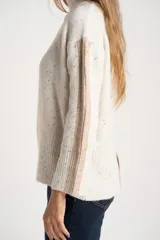 Polera de punto con diseño oversize, cuello alto y mangas largas con paneles laterales en contraste. Presenta un tejido jaspeado con motas multicolores y detalles de lurex.