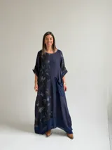 Vestido largo azul oscuro con diseño asimétrico que combina un lado liso con un lado estampado de hojas, manga corta y bolsillo frontal aplicado.