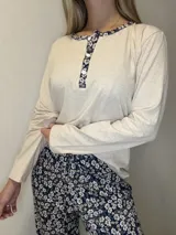 Pijama de algodón compuesto por una remera de manga larga en color beige melange con escote redondo, cartera de botones y detalles de tela floreada en el cuello y tapeta, y un pantalón largo con estampado floral en tonos azules.