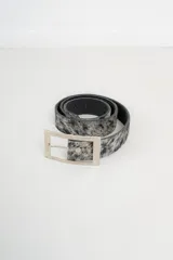 Cinto de cuero con estampado animal print de vaca en tonos marrón y blanco, con hebilla metálica dorada.