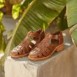 Sandalias franciscanas de cuero color marrón, con diseño tejido de tiras en la capellada, taco cuadrado bajo y tira ajustable con hebilla en el tobillo.