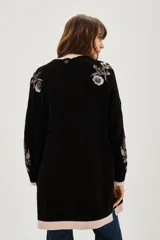 Cardigan negro de punto con bordados florales y aplicaciones de lentejuelas. Presenta terminaciones en tejido acanalado de color beige en los puños, el ruedo y a lo largo de la apertura frontal.