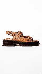 Sandalias de mujer color marrón con suela track gruesa y negra. Presentan tiras de cuero texturizado con hebillas metálicas ajustables en el empeine y tobillo.