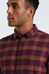 Camisa de manga larga confeccionada en tela de franela con estampado de cuadros en tonos bordó, naranja y azul. Presenta cuello con botones, cierre frontal abotonado y bolsillo en el pecho.