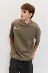 Remera de corte oversize color blanco tiza, de manga corta y cuello redondo, con pequeño estampado gráfico azul en el pecho.