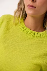 Blusa verde lima con textura arrugada, cuello redondo con volantes y mangas largas con puños elásticos.