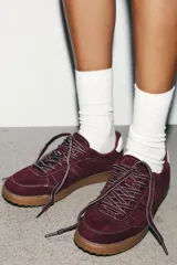 Zapatilla deportiva de gamuza color bordó con suela de goma y costuras en contraste blanco. Presenta detalle de talón en color blanco y cordones bicolores.